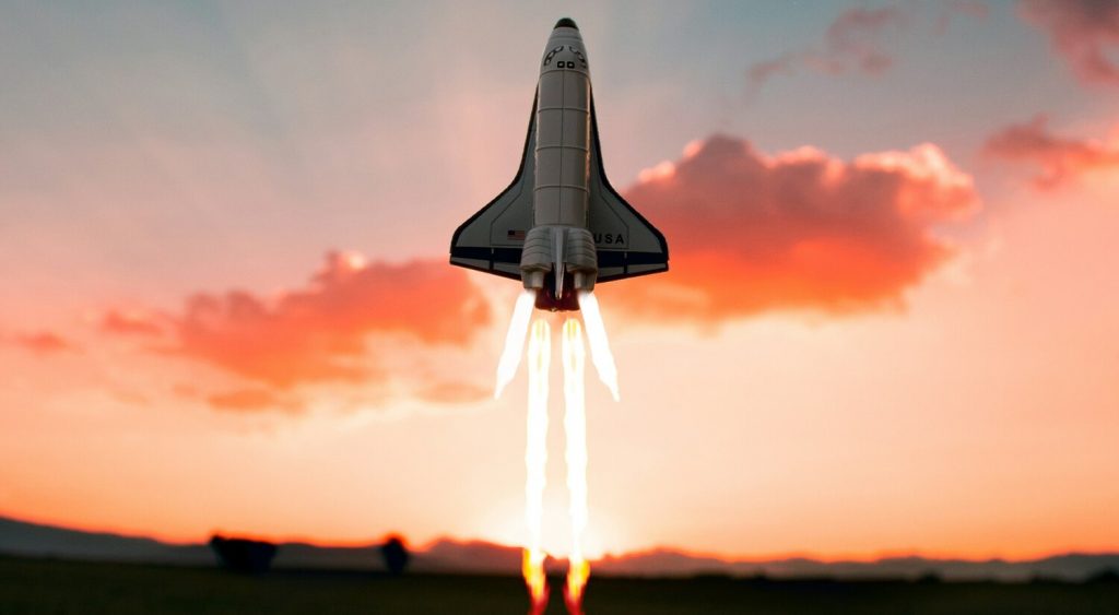 Eine Rakete startet gen Himmel, der im Hintergrund orange-rosa leuchtet.